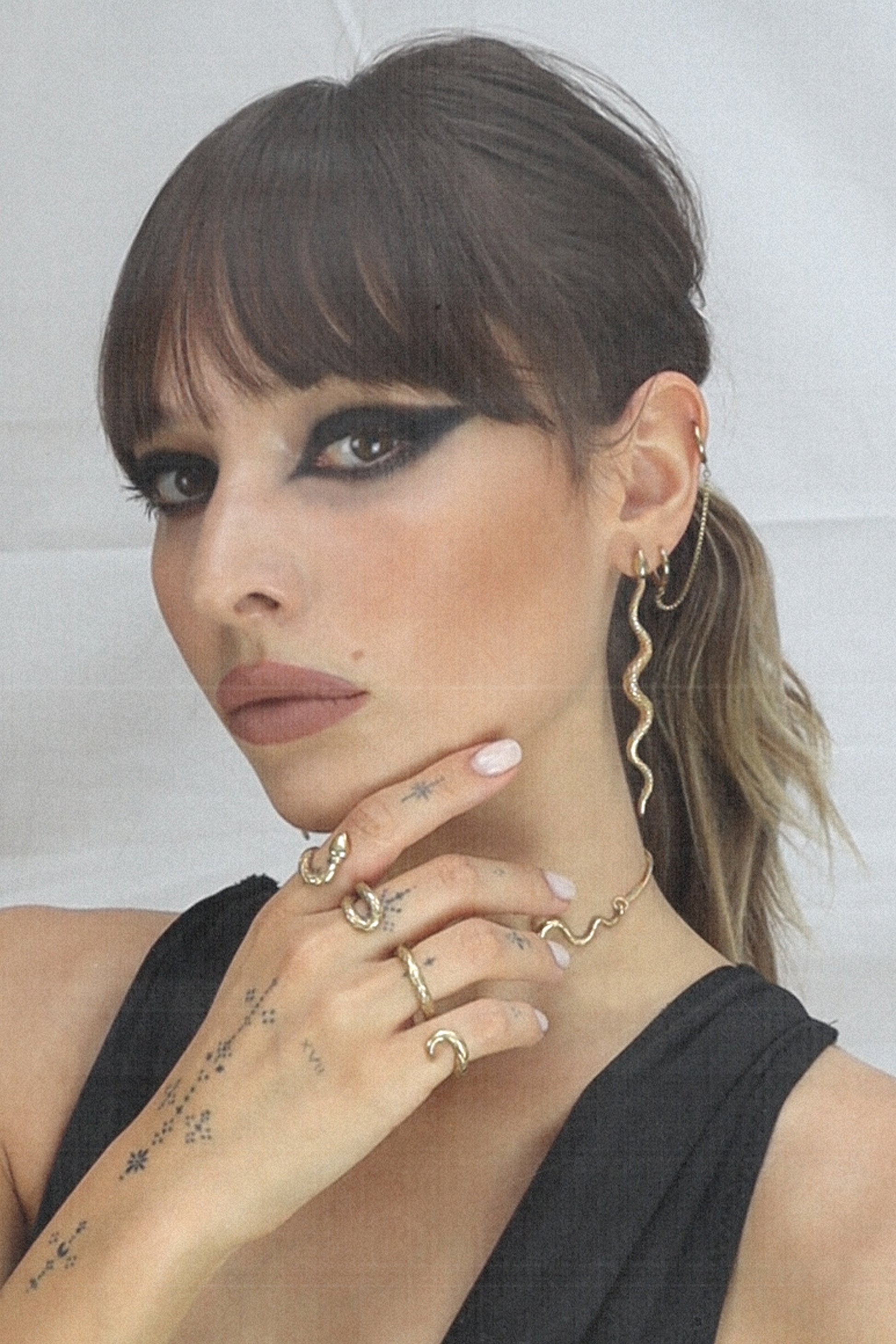 girl wearing 4 fingers ring resembling a snake, with hand tattoos, bold black makeup and a black low cut swimsuit. Vintage photocopy effect picture.