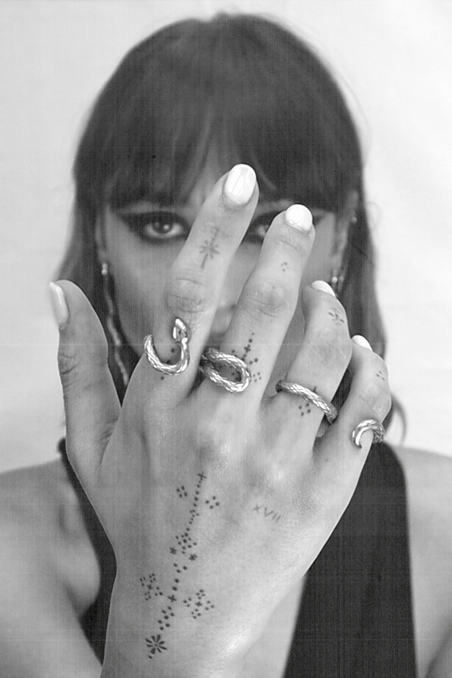 girl wearing 4 fingers ring resembling a snake, with hand tattoos, bold black makeup and a black low cut swimsuit. Black and white picture.