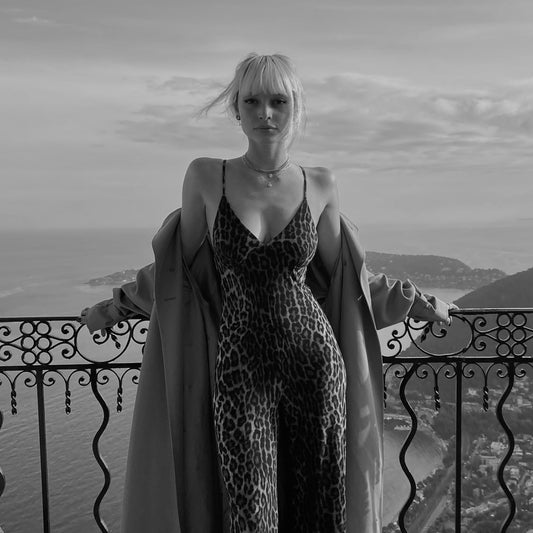 black and white picture of the designer, 25 years old girl wearing a leopard print romper from Norma Kamali, Burberry long coat, with a view on the coast of Monte Carlo.